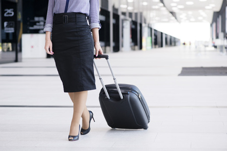 Business woman in formal clothing walking with wheeled bag at airport terminalの写真素材