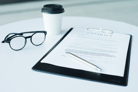 A pair of women's glasses and a pen lying on top of a white sheet of paper on wooden surface. The sheet has a coffee stain. Copy space in lower and right part of image. High angle view.の写真素材