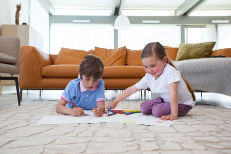 Little boy and girl drawing with color pencils on the floor playing togetherの写真素材