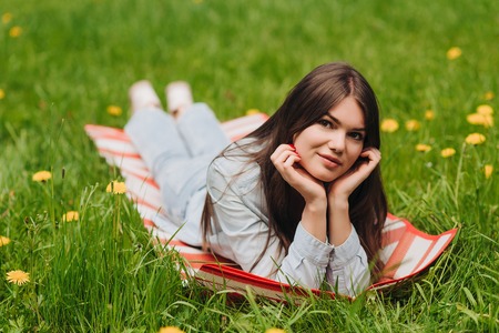 Beautiful young woman laying on grass with dandelion flowers in parkの写真素材