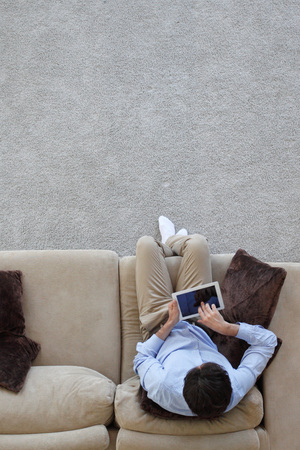 Man surfing on tablet on a couch at home, top viewの写真素材