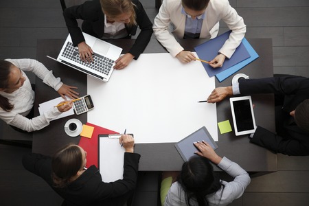 Business workplace with people, cup of coffee, digital tablet, smartphone, papers and various office objects on tableの写真素材