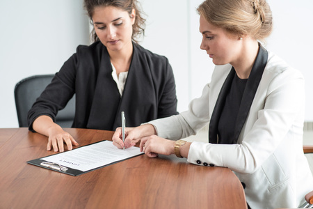 Two business women signing a document at conference tableの写真素材