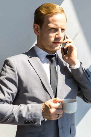 Portrait of a young business man talking on smartphone and holding cup of coffeeの写真素材