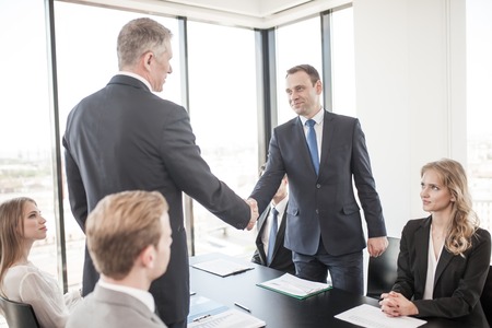 Handshake of business people at meeting in ofice , team sitting around table and discussing...