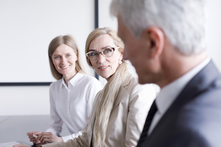Business people sitting in a row and working, focus on mature woman in glassesの写真素材