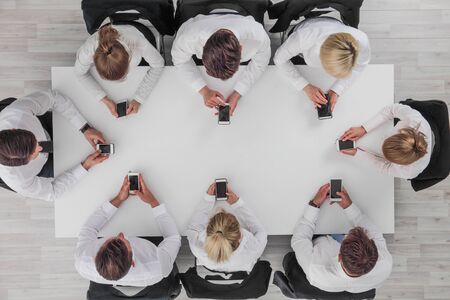 Top view of business people sitting around the table and using smartphones with blank screenの写真素材