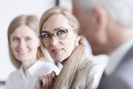 Business people sitting in a row and working, focus on mature woman in glassesの写真素材
