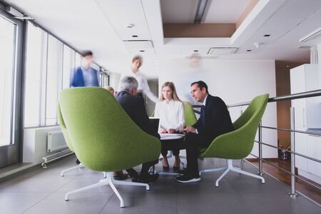 Business people sitting together on armchairs in office hall and having a discussionの写真素材