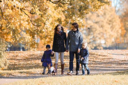 Happy smiling family of parents and children walking together holding hands in autumn parkの写真素材