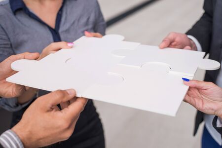Hands of business people holding white puzzleの写真素材