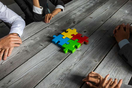 Business people team sitting around meeting table finishing assembling color jigsaw puzzle pieces unity cooperation ideas conceptの写真素材