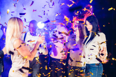 Having fun together. Group of beautiful young happy multi race people dance holding champagne in golden confetti and smiling nightlife new year celebration partyの写真素材