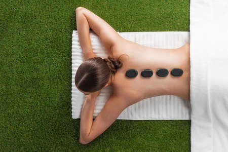 Natural body care concept, woman at spa massage with hot stones lying on grass, top viewの写真素材