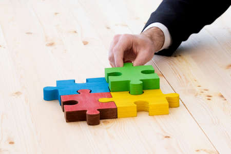 Business man assembling four color jigsaw puzzle pieces problem solution ideas concept