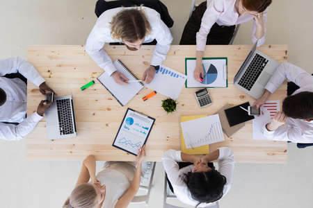Business people brainstorming at office desk analyzing financial reports and pointing out financial...