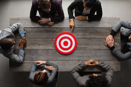 Team of business people sitting around red target at meeting tableの写真素材