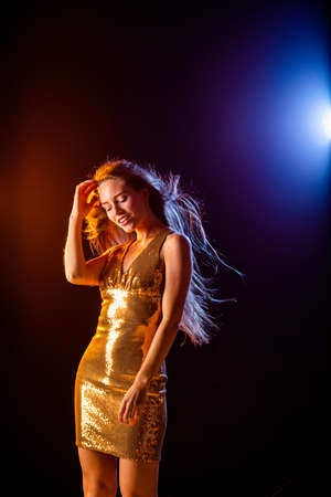 Beautiful girl in Golden dress dancing on black background, color lightsの写真素材