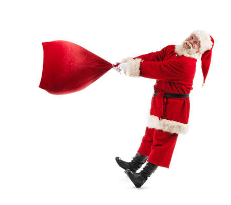 Santa Claus with a big bag on isolated white background. Funny Santa throw large sack of Christmas gifts. Cheerful Santa Claus spin bag with gifts.の写真素材
