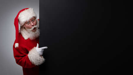 Santa Claus pointing at black paper billboard with copy space for text, surprised facial expressionの写真素材