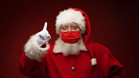 Santa Claus in red medical mask pointing finger up restriction covid christmas celebration conceptの写真素材