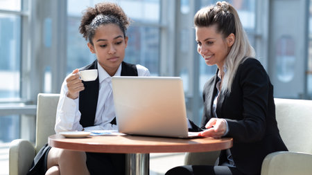 Two business women in modern office building cafe working with laptopの写真素材