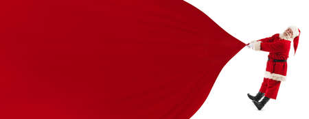 Santa Claus pulling huge bag of gifts isolated on white with copy space for text, big red banner backgroundの写真素材