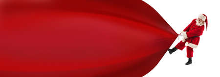 Santa Claus pulling huge bag of gifts isolated on white with copy space for text, big red banner backgroundの写真素材