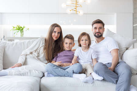 Happy family of parents with children sitting together on sofa at homeの写真素材