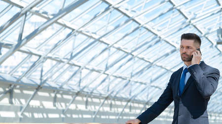 Business background of mature man talking on phone in modern office lobby, copy space for text...