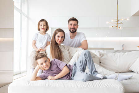 Happy family of parents with children sitting together on sofa at homeの写真素材