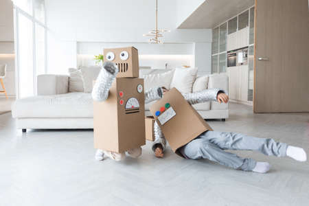 Happy two children playing robots at home, children wearing handmade moving box costume of cardboardの写真素材