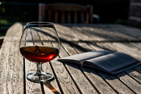 Glass of Cognac with a book on wooden surface at garden (natural light). Beverage Concept.の写真素材