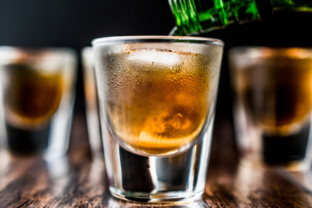 Pouring Whiskey Shots with ice on dark wooden surface. Beverage Concept.