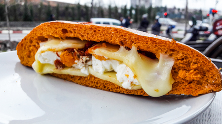 Sandwich with melted feta cheese and dried tomato in the city. (fast food concept.)の写真素材