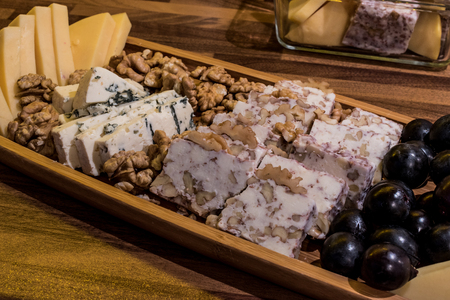 Cheese plate: Emmental, Camembert cheese, blue cheese, cheddar, grape, walnuts on wooen surfaceの写真素材