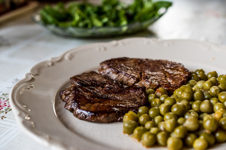 Tenderloin Steak with peas and green salad at kitchen table. Organic Food.の写真素材
