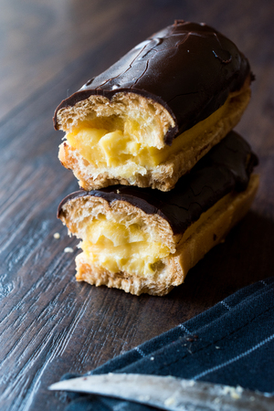 Half Cut Cream Filled Chocolate Eclairs on Dark Wooden Surface. Dessert Concept.