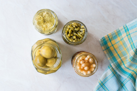Jars of Pickled Vegetables Green and White Asparagus, Artichoke Heart and Unripe Green Almond Pickles in Glass Bottle. Organic Food.の写真素材