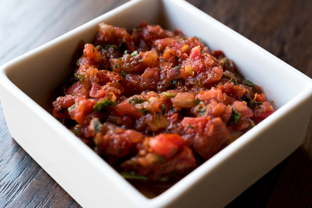 Turkish Meze Acili Ezme or acuka made with fresh tomatoes and spices in square ceramic bowl....