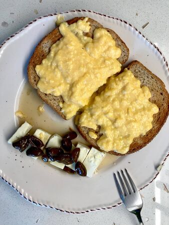 Homemade Creamy Scrambled Eggs in Breakfast Plate with Toast Bread, Cheese and Pistachio Jam /...