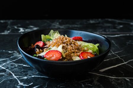 Buckwheat Salad with Strawberry Slices and Green Leaves in Black Bowl on Dark Granite Surface. Organic Fresh Food.の写真素材