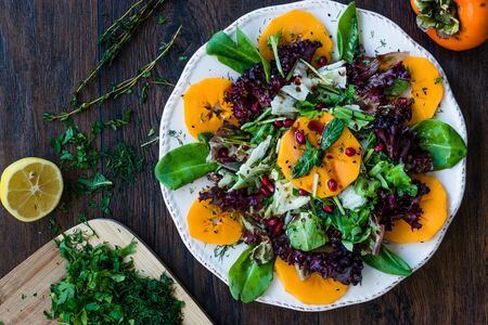 Persimmon Fruit Salad with Pomegranate, Lollo Rosso Lettuce, Rocket Arugula or Rucola and Mint Leaves. Organic Food.の写真素材