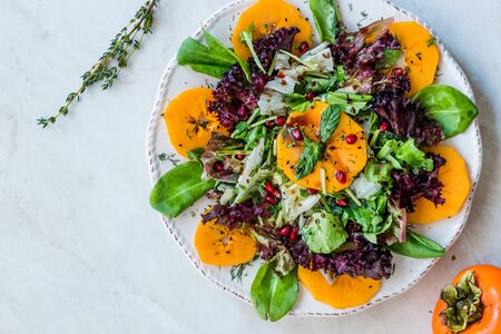 Persimmon Fruit Salad with Pomegranate, Lollo Rosso Lettuce, Rocket Arugula or Rucola and Mint Leaves. Organic Food.の写真素材