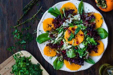 Persimmon Fruit Salad with Pomegranate, Lollo Rosso Lettuce, Rocket Arugula or Rucola and Mint Leaves. Organic Food.の写真素材
