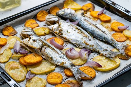 Baked Fish Bluefish with Sweet Potatoes on Oven Tray with Baking Paper Sheet / Lufer. Seafood.の写真素材