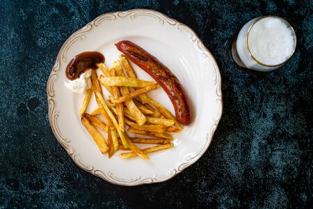 Homemade Sausage with Skinny French Fries Potatoes in Plate with Glass of Beer also called Peruvian Salchipapa. Fast Food.の写真素材