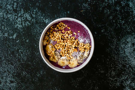 Take Away Vegan Food Acai Bowl with Almond Milk, Peanut Butter, Banana, Buckwheat Granola, Chia Seeds and Chocolate Pieces in Carton Bowl. Healthy Organic Food.の写真素材