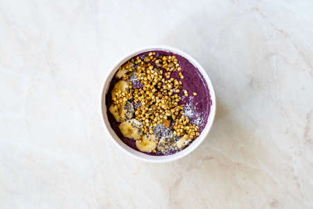 Take Away Vegan Food Acai Bowl with Almond Milk, Peanut Butter, Banana, Buckwheat Granola, Chia Seeds and Chocolate Pieces in Carton Bowl. Healthy Organic Food.の写真素材