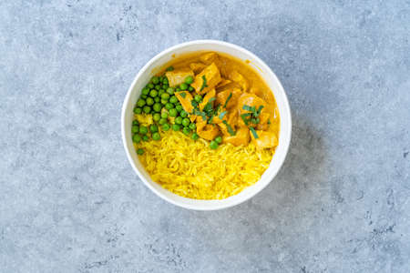 Take Away Indian Street Food Tikka Masala with Chicken, Curry Basmati Rice, Green Peas and Coconut Milk Sauce in Plastic Container Bowl.の写真素材